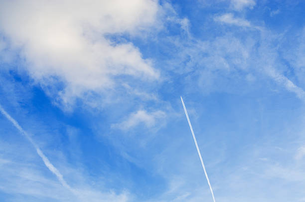 Airplane contrail soaring through a bright blue sky with scattered white clouds