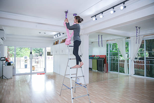 A person standing on a ladder, carrying out tasks with white cabinets in an indoor setting.