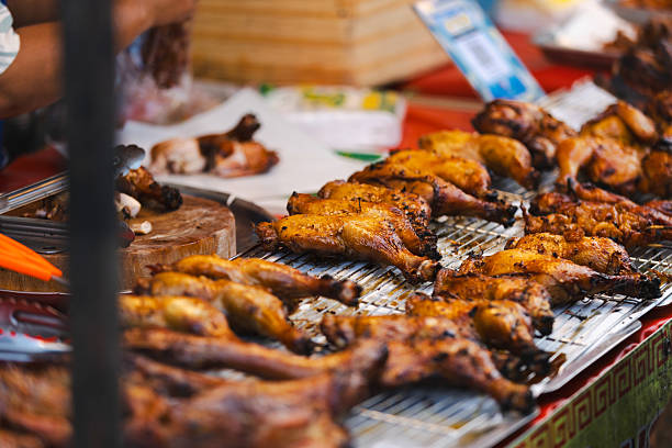 Asian street food market.Cooked barbecue chicken legs are selling on street food market stand.Phuket Island - Thailand.