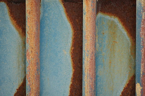 Close-up of a rusty metal wall with peeling blue paint and corrosion, showcasing industrial textures and decay.