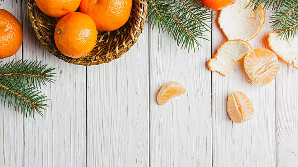 istock Tangerines in a straw basket with spruce branches on a white wooden table. 2251377184