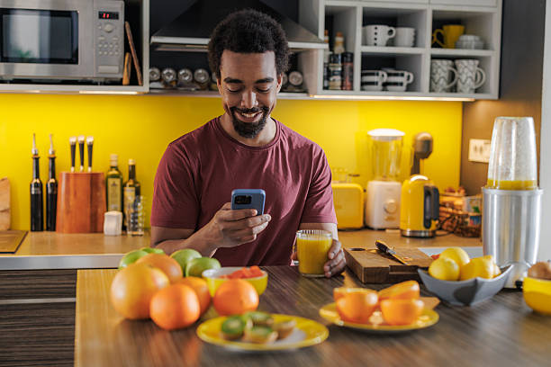 istock Young man smiling while using smartphone at the home kitchen counter with fresh fruit and vegetables 2251378572