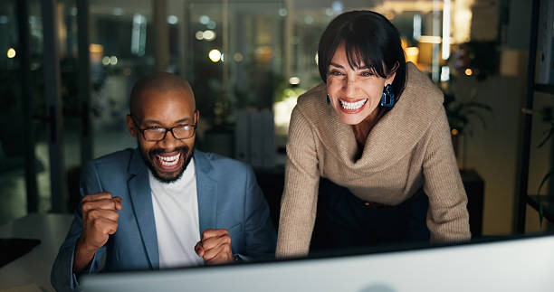 istock Team, success and computer with business people in office for night, project approval and partnership. Collaboration, winner and online feedback with man and woman in agency for overtime and bokeh 2251378655