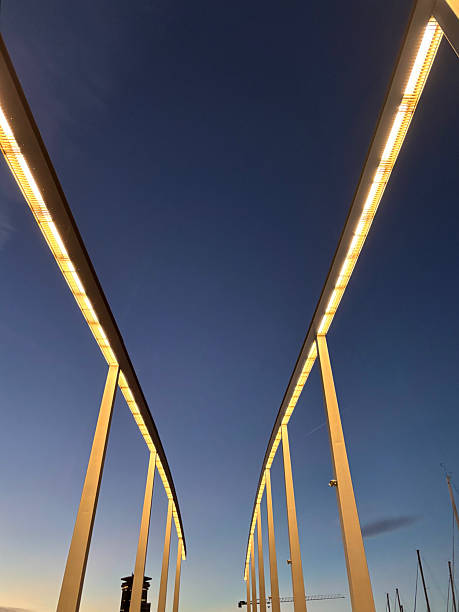 Modern Rambla de Mar bridge with glowing light strips creating a striking vanishing-point perspective against the deep blue evening sky over Barcelona's waterfront harbor