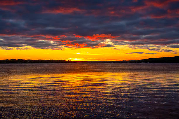 The sun is just seconds from setting, with its rays reflecting on the water in tones of yellow and orange.  A bank of cumulus clouds cover much of the sky, with the suns rays turning them into an ominous display of reds and blues.