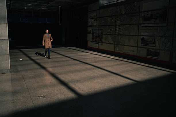 A businessman walks through a large hall where strong sunlight creates long, dramatic shadows across the floor. Dressed in professional attire, he moves with calm purpose, emphasizing themes of urban routine, modern architecture, and the quiet moments within a busy business day.