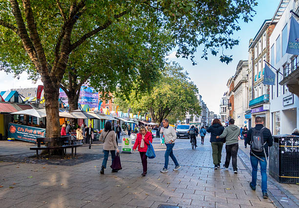 Norwich, Norfolk, United Kingdom: October 14, 2024:  People on Gentlemans Walk in Norwich, Norfolk, Eastern England on a warm October day. The famous Norwich Market is on the left.