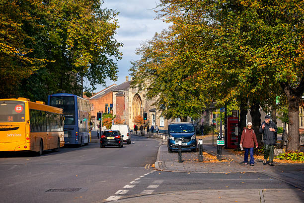 Tourists and traffic in Tombland, an ancient part of the old city of Norwich in Norfolk, Eastern England. Gates to the famous Norwich Cathedral are on the right. Tombland, which has nothing to do with tombs, was once the original market place in this picturesque city