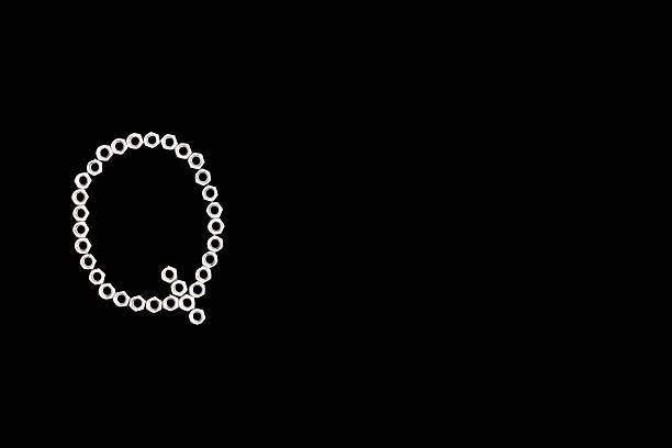 A ring of hex nuts is completed with a small diagonal segment, creating a distinctive capital Q on a dark background. The circular form and tail detail give the letter a dynamic, almost technical symbol quality. This industrial alphabet photograph fits topics such as quality control, technology, engineering and logistics. Its clear silhouette and wide copy space make it an excellent element for branding, presentation slides, infographics or digital interfaces.