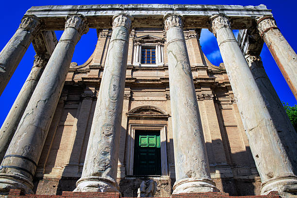 Slide photograph from 2002 capturing the Roman Forum, Rome. This well-preserved ancient structure features towering Corinthian marble columns, a classical entablature, and a raised podium accessed by stone steps. Surrounded by light vegetation and set against a clear blue sky, the image highlights the grandeur and architectural precision of Imperial Roman design. The analog film texture adds a nostalgic quality, ideal for editorial, educational, and travel-themed creative use. A timeless view of Roman heritage and classical engineering.
