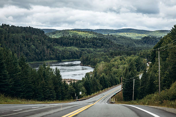 Scenic highway running through a lush green forest with a wide river and rolling hills near La Tuque in Quebec, Canada