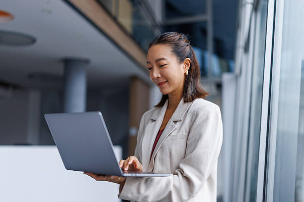istock Businesswoman standing in office using laptop smiling 2251420096