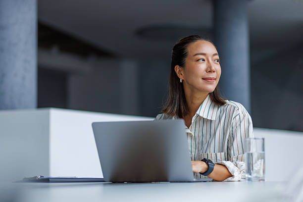 istock Asian businesswoman looking away and thinking while working on laptop 2251420148