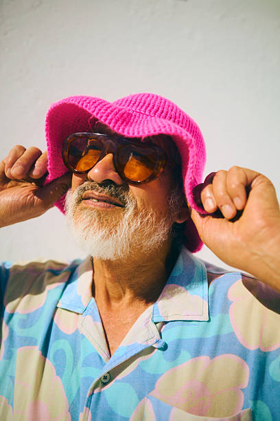 Senior man smiling, wearing a colorful shirt and modern accessories against a bright background