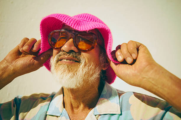 Senior man smiling, wearing a colorful shirt and modern accessories against a bright background