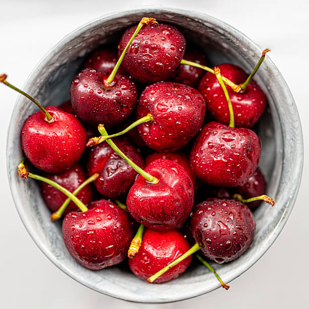 Fresh red cherries in the bowl with water drops overhead on white