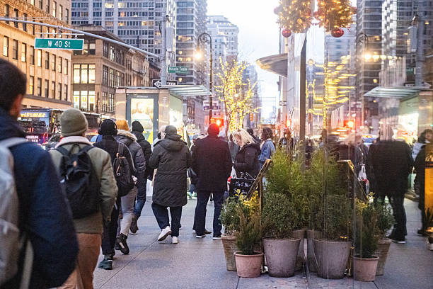 New York City, NY, USA - December 4th, 2025: Many people walk towards their destination along the 6th Avenue sidwalk in the Garment District at rush hour.