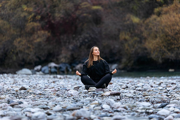 istock Woman practicing meditation on rocky riverbank, surrounded by nature, showcasing tranquility and mindfulness in a serene outdoor environment with calming water flow 2251427965