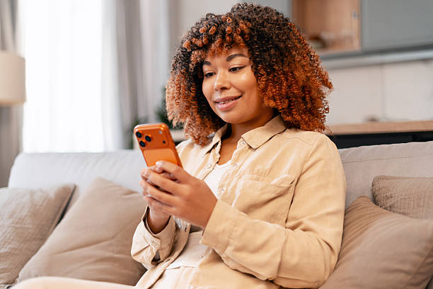 istock Young adult woman relaxing on sofa, smiling while using modern smartphone 2251437933