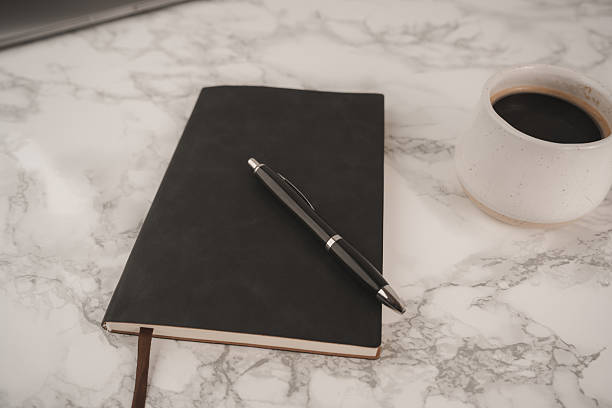 istock A black notebook and pen rest on a smooth marble table beside a white coffee cup filled with dark coffee. This scene captures a peaceful moment for creativity 2251439816
