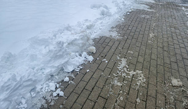 Snow piled next to a brick pathway in a winter setting, highlighting the contrast between the white snow and textured pavement, ideal for seasonal or weather-related themes.