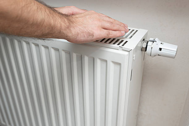 istock A person checking a heater with their hand on the surface, ensuring warmth in a home environment. The setting suggests domestic comfort and maintenance practices. 2251445236