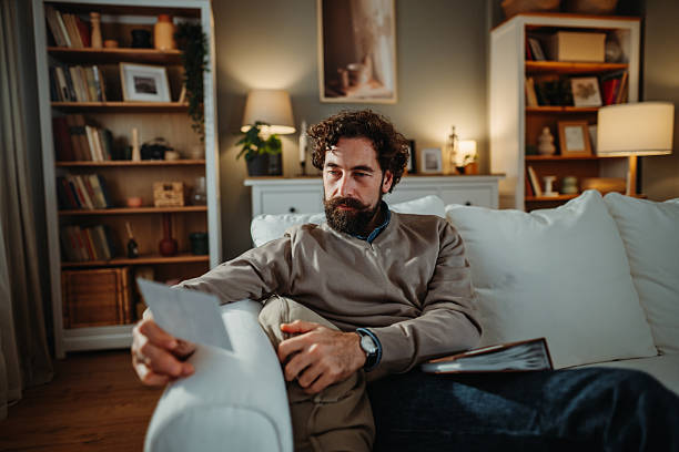 istock Man reminiscing memories looking at old photographs on couch 2251447172