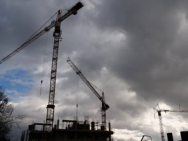 Silhouetted tower cranes at construction site against dark dramaticsky. Industrial development with heavy machinery and unfinished buildingstructure.