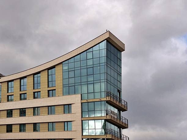 Modern office building with curved glass facade and beige horizontalpanels under an overcast sky, a low-angle view of contemporary Europeanarchitecture.