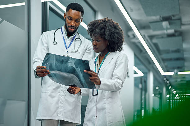 Two African-American doctors carefully examining a patient's x-ray film, collaborating on a medical diagnosis in a modern hospital hallway, representing teamwork and healthcare