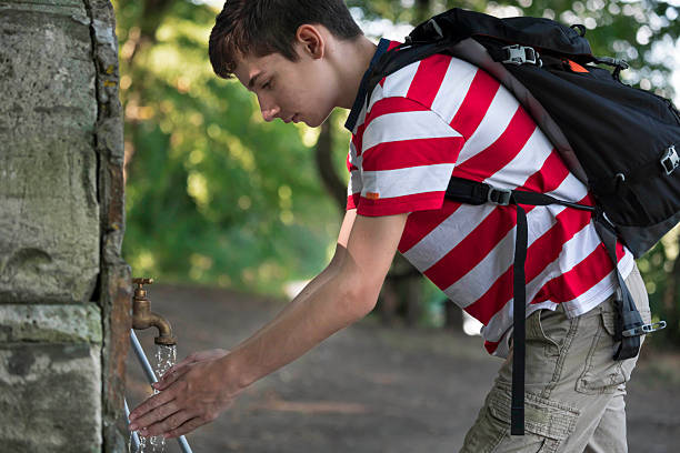 A young tourist washing his hands with fresh water from an outdoor drinking fountain, enjoying a moment of hydration and refreshment in nature.