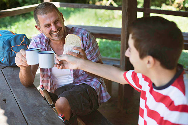 istock Cheerful father and son clinking enamel mugs during forest lunch 2251462979