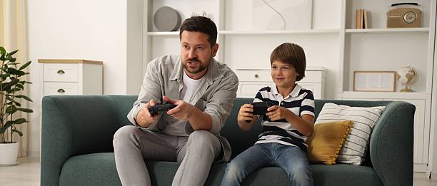 istock Father and son with controllers playing videogame on sofa at home 2251463645