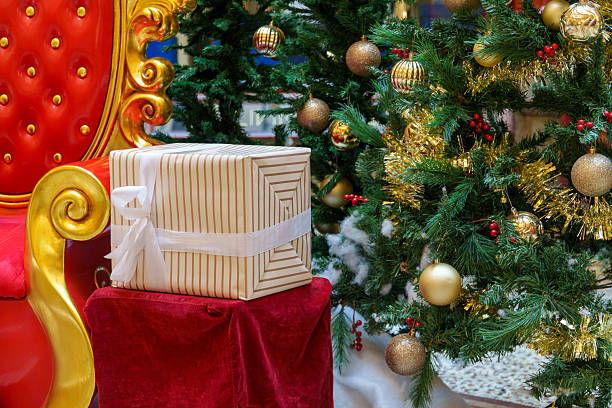 istock Luxurious Red and Gold Throne Adorned with a Striped Gift Box Next to a Glittering Christmas Tree Display 2251466106