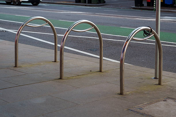 A row of three modern metal bicycle racks is pictured on a city sidewalk alongside a street with a dedicated green cycling lane.