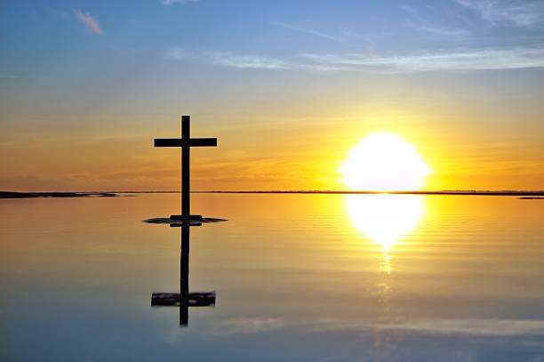 Dark cross on a beach with a wonderful sunset sky in the background. Also still flat reflective Water.