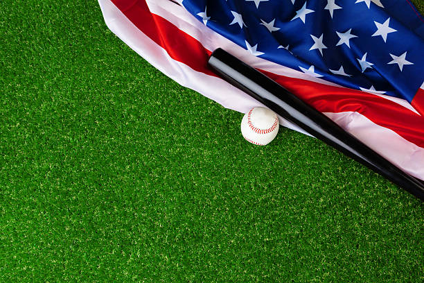 istock Baseball bat and ball with american flag on grass 2251475629
