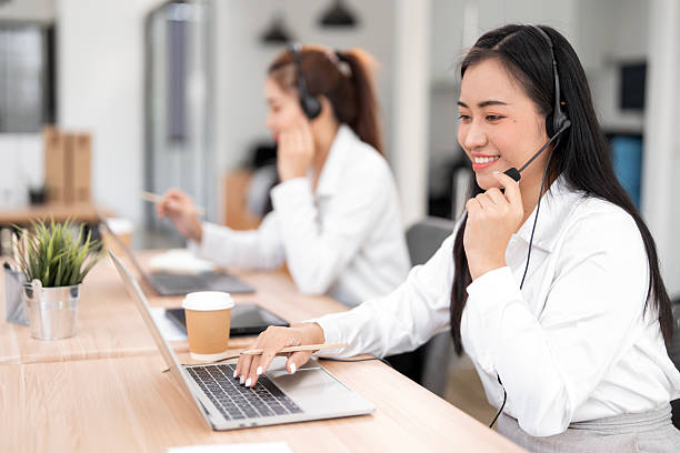 istock Smiling Asian woman wearing a headset with a microphone, providing excellent customer support or attending a virtual meeting at her laptop in a modern call center or office. 2251478254