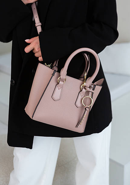 istock Small taupe leather handbag with gold details, structured design, styled with a black blazer and white trousers 2251479735
