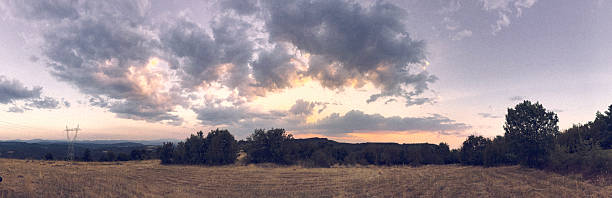 Tranquil sunset scene with dramatic clouds over expansive rolling hills and dry grasslands. Trees and distant mountains enhance the natural beauty of the landscape