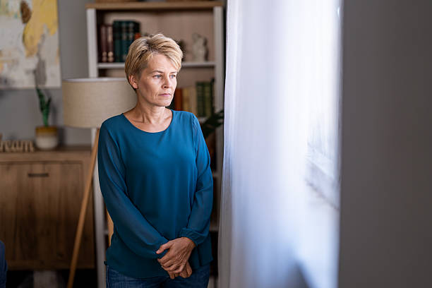 Mature woman standing alone at home feeling thoughtful and sad