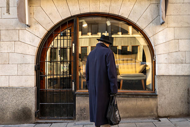 Stockholm, Sweden Nov 14, 2025 A senior man with a hat and an overcoat  walks past antique furniture store.