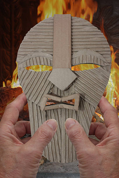 Hands holding a cardboard masquerade mask against the backdrop of a burning fire.Note: I certify that I am the sole author and creator of the masquerade mask shown in this image.