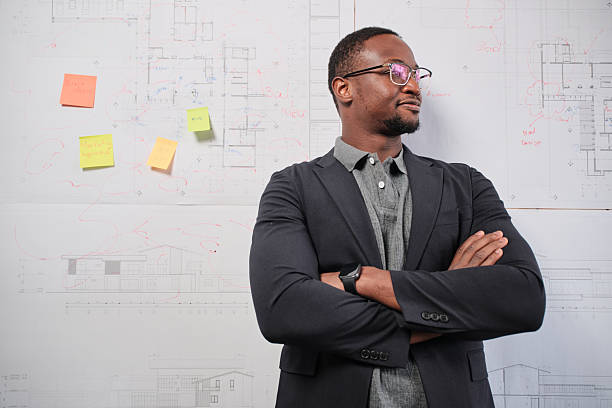 One smart young Black male architect in suit standing with design work on board, building construction blueprint with business concept ideas in studio company, happy and confident in presentation.