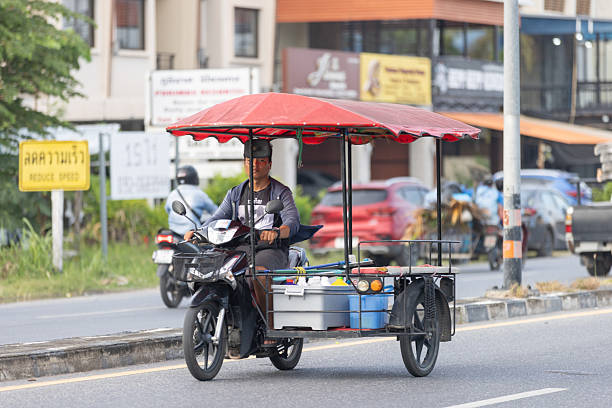 11 December 2025, Phuket Island - Thailand.A man rides him tricycle along the road, adapted as a mobile stall for local markets in Thailand. Many markets operate on specific days, requiring vendors to travel between locations, and this mobility allows them to reach different communities throughout the week.