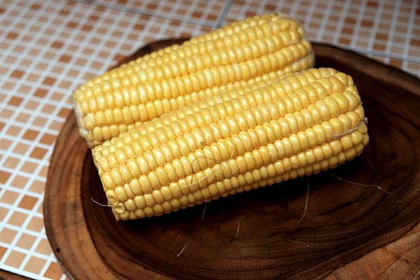 Fresh raw yellow ​​sweet corn on a wooden chopping board. healthy traditional snack, suitable for themes like healthy eating, summer produce, agriculture, vegan food, and natural lifestyle.