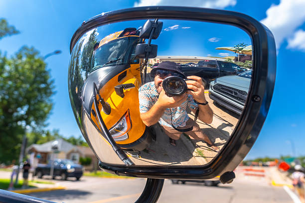 Photographer is taking a selfie reflected in the mirror of a yellow school bus, capturing the unique scenery of drumheller, a city known for its dinosaur fossils and otherworldly landscapes