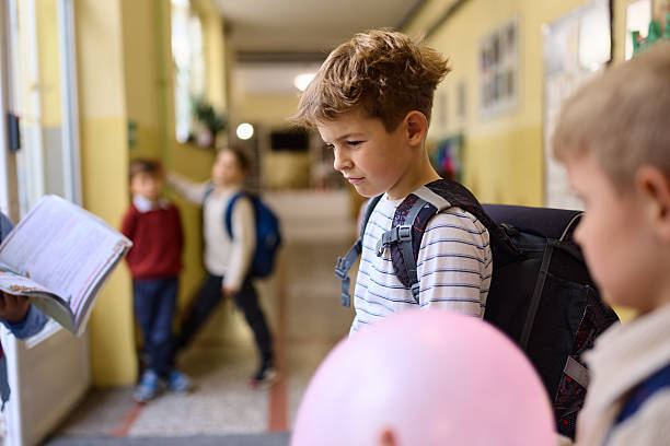 Displeased schoolboy standing alone in a hallway of elementary school.