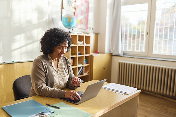 istock Smiling mature teacher working on laptop in the classroom. 2251513678