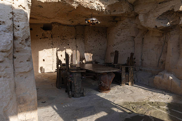 Cozy stone-walled cave interior with wooden dining table and chairs bathed in natural light, offering a unique and atmospheric gathering space.